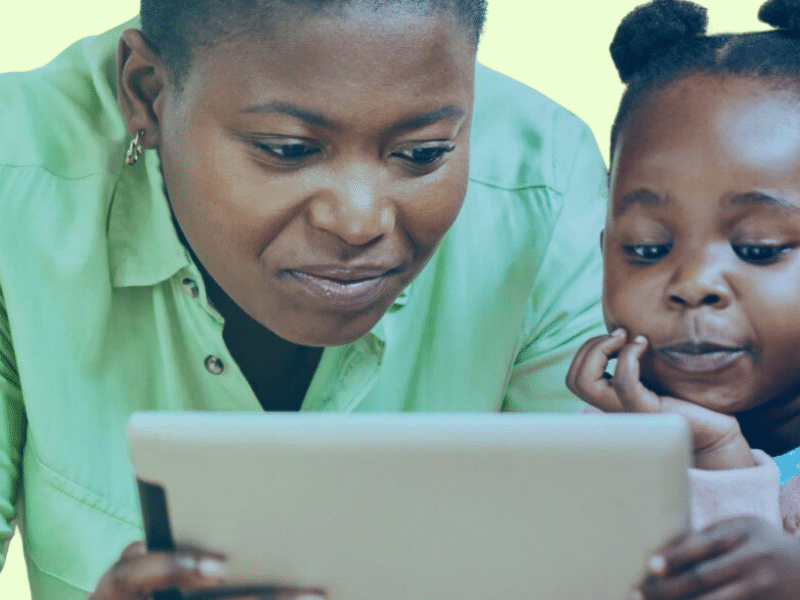 A caregiver and a child look intently at a tablet they are holding together.