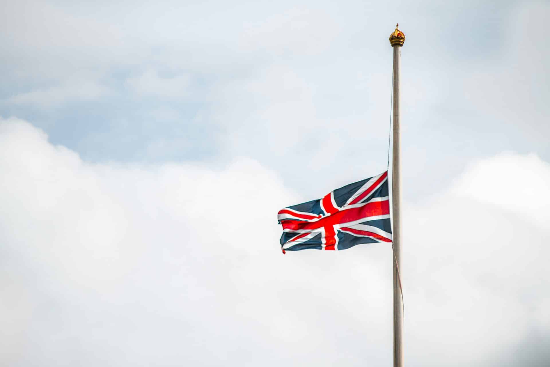 A UK flag is flying half-mast and waving in the wind.