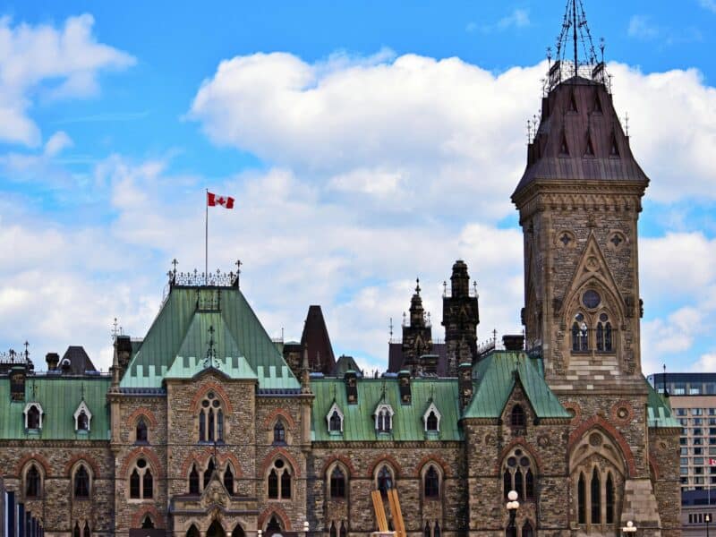 Parliament hill, Canada’s Parliament building, with a Canadian flag flying in the cloudy sky