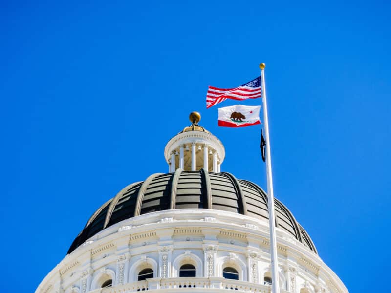 The US and the California state flag waving in the wind in front of the dome of the California State Capitol, Sacramento, California