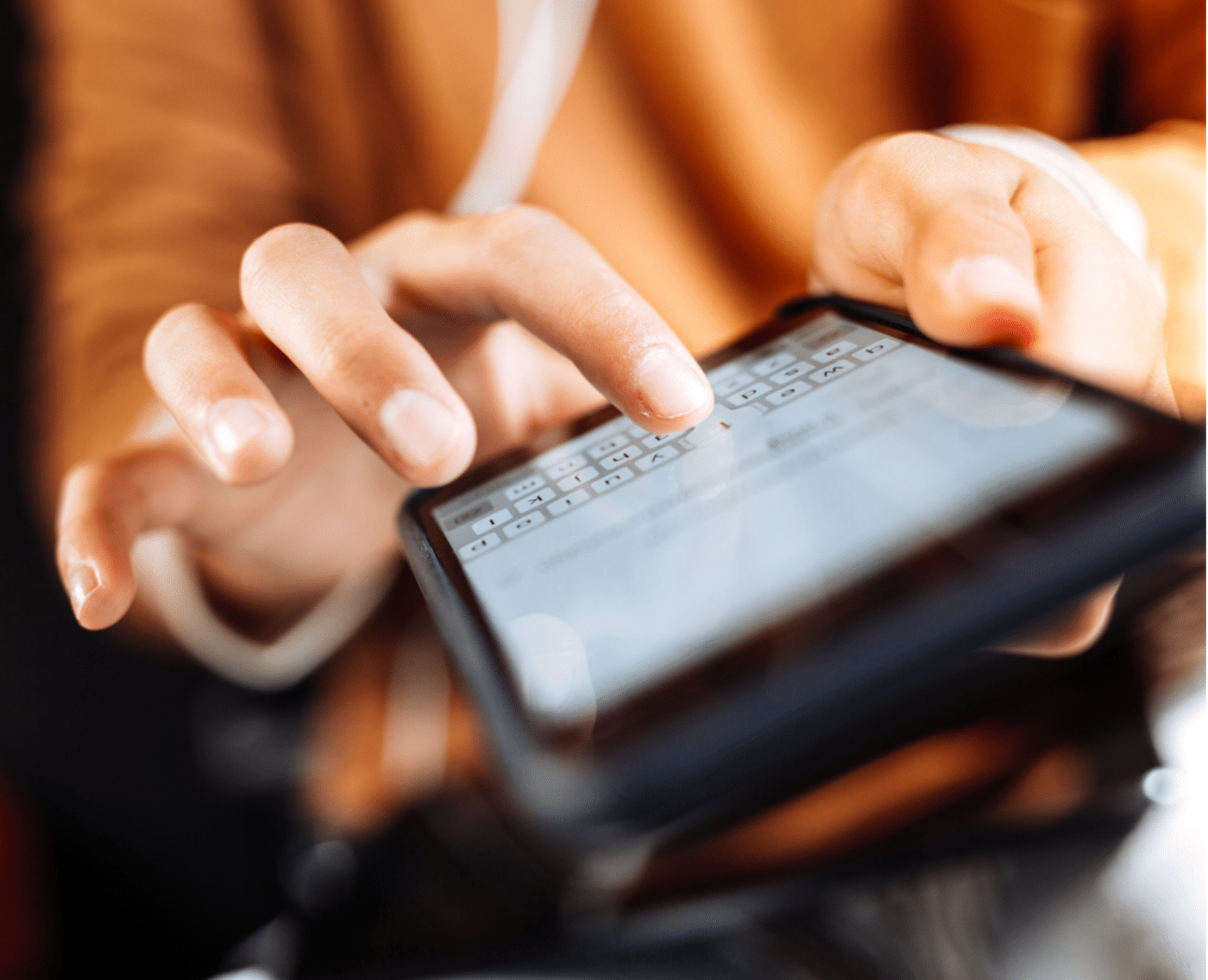 A close-up image of a person's hands typing on a smartphone. The fingers are in motion, interacting with the on-screen keyboard, which is slightly blurred. The person appears to be focused on the device, with the screen displaying text input. The background is blurred, drawing attention to the hands and the phone.