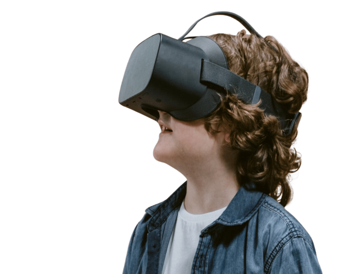 A young child with curly hair is wearing a virtual reality headset and smiling. They are dressed in a denim jacket and a white shirt, standing against a plain beige background.