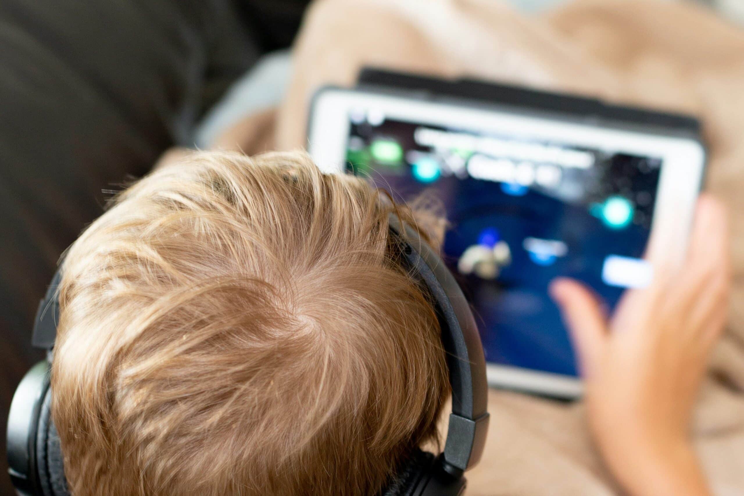 Boy in a white shirt playing a game on a white tablet computer while sat on a sofa. 