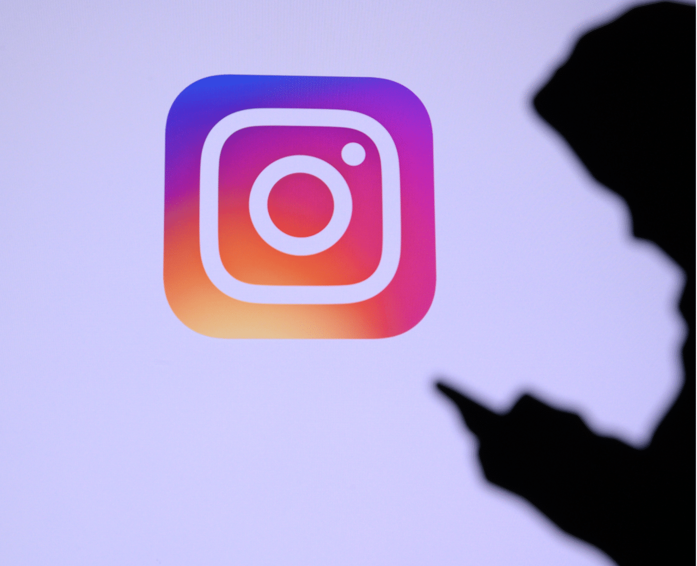 A wider shot showing the large Instagram logo on a screen. In the foreground, there is a silhouette of a person holding and using a smartphone, with the focus primarily on the logo. This is the full version of the close-up shown above.