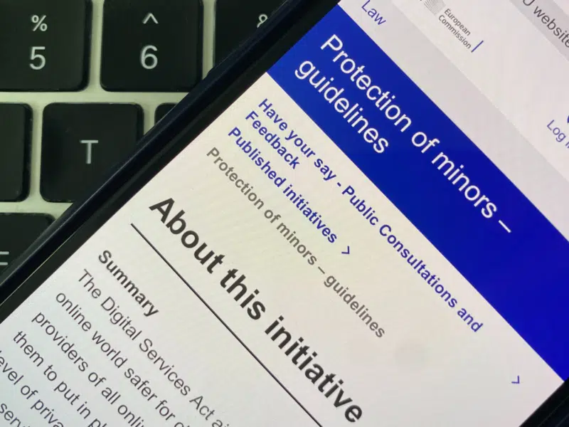 A smartphone screen displaying a webpage from the European Commission about guidelines on the protection of minors under the Digital Services Act. The page includes a section titled 'About this initiative'.