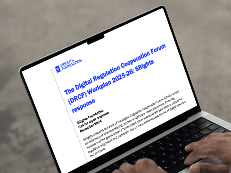 A close-up shot of a laptop screen displaying a document titled 'The Digital Regulation Cooperation Forum (DRCF) Workplan 2025-26: 5Rights response.' The document header features the 5Rights Foundation logo, and below, the text begins with '5Rights Foundation Call for input response' dated November 2024. Hands are visible on the laptop’s keyboard, suggesting someone is reviewing or typing on the document.