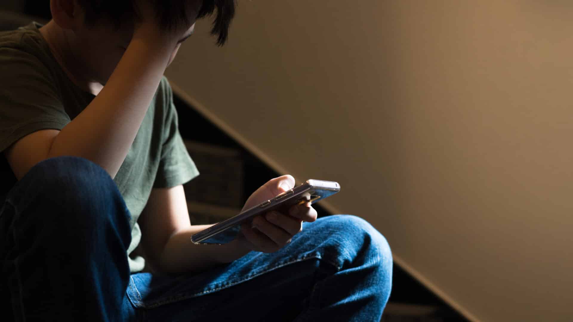 teenage boy sitting on stairs upset with a phone in hand.