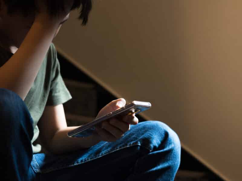 teenage boy sitting on stairs upset with a phone in hand.