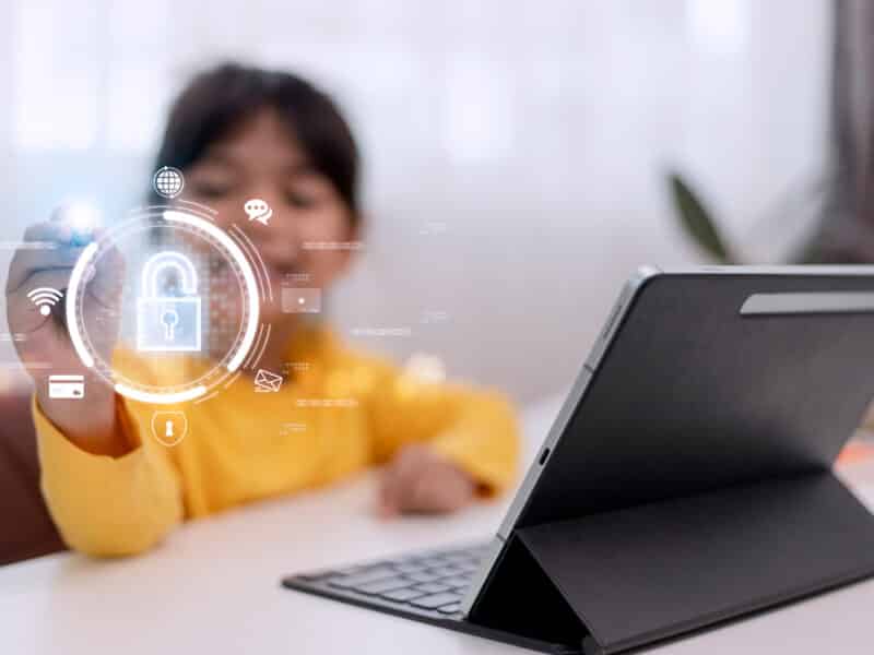 Little girl using laptop at home. icon of internet blocking app on foreground