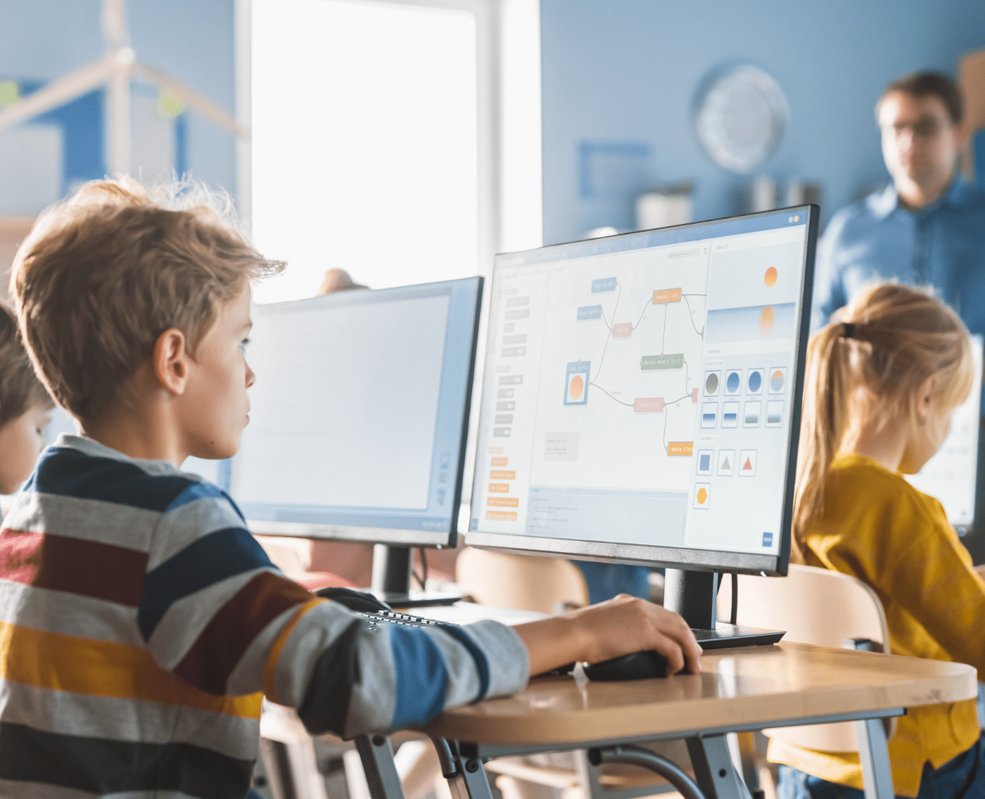 A classroom of young students working on desktop computers, with educational software visible on the screens. A boy in a striped shirt and a girl in a yellow top are prominently shown, deeply engaged in a digital activity. A teacher stands in the background, observing the class. 