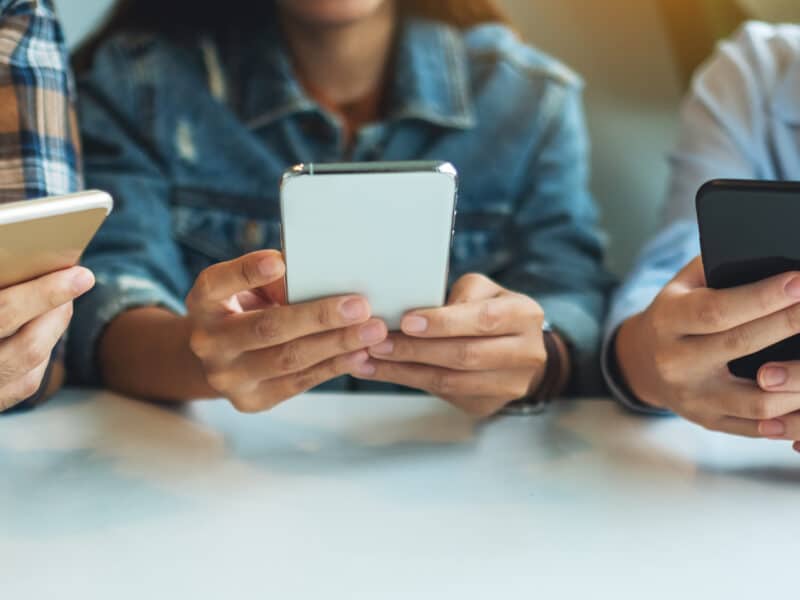 Group of young people using and looking at mobile phone while sitting together