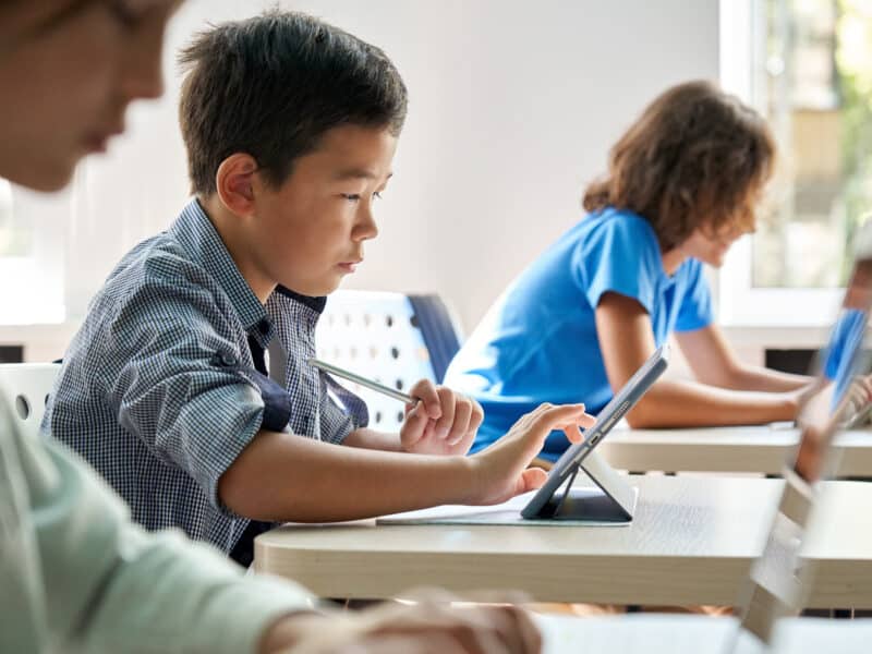 school boy using digital tablet at class in classroom. Attentive junior school student learning online virtual education digital program app tech during stem computer science lesson.