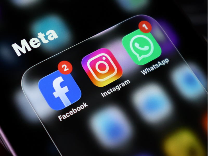 Close-up of a smartphone screen showing the "Meta" logo overlaid on the Facebook, Instagram, and WhatsApp app icons, each displaying unread notification badges.