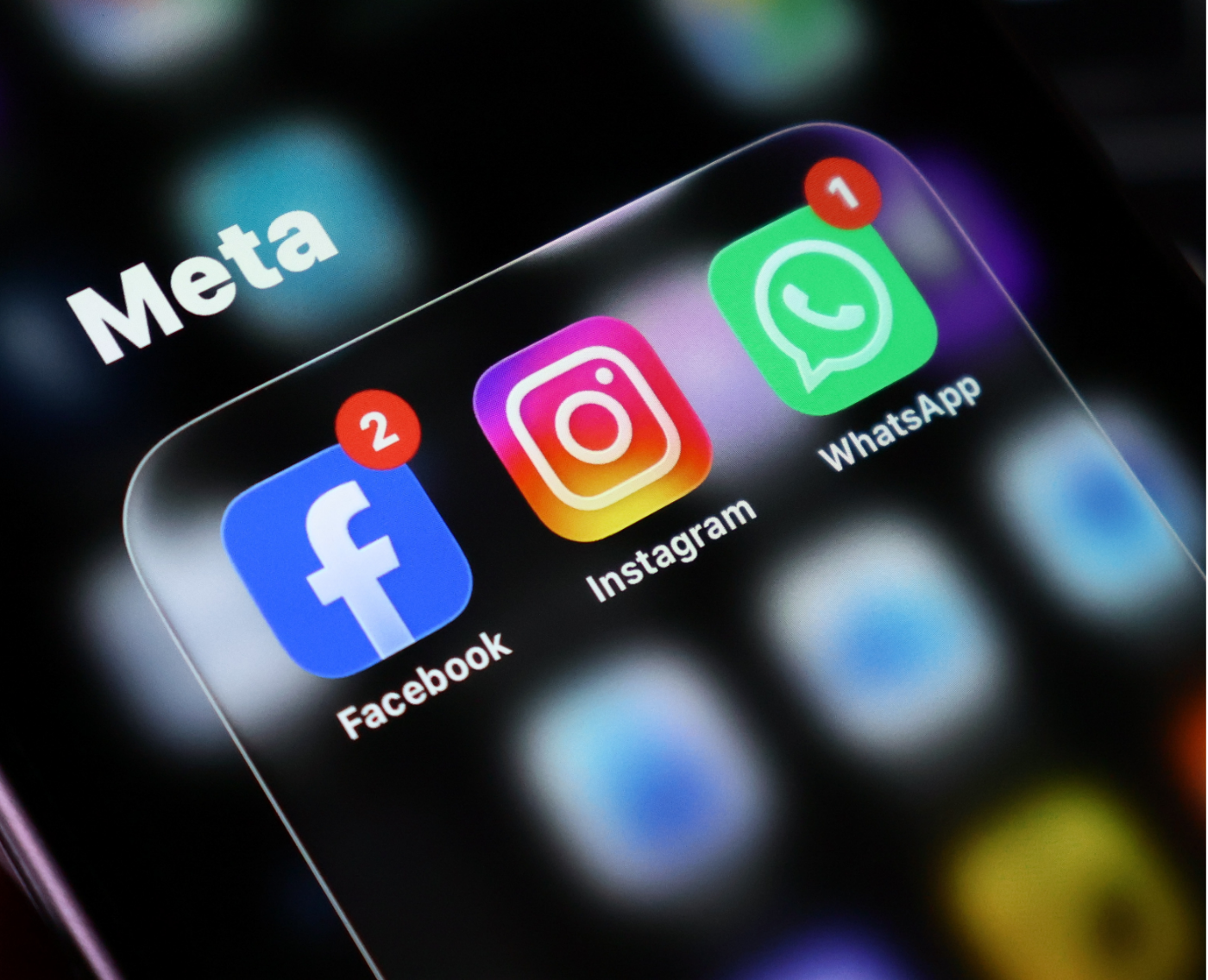 Close-up of a smartphone screen showing the "Meta" logo overlaid on the Facebook, Instagram, and WhatsApp app icons, each displaying unread notification badges.