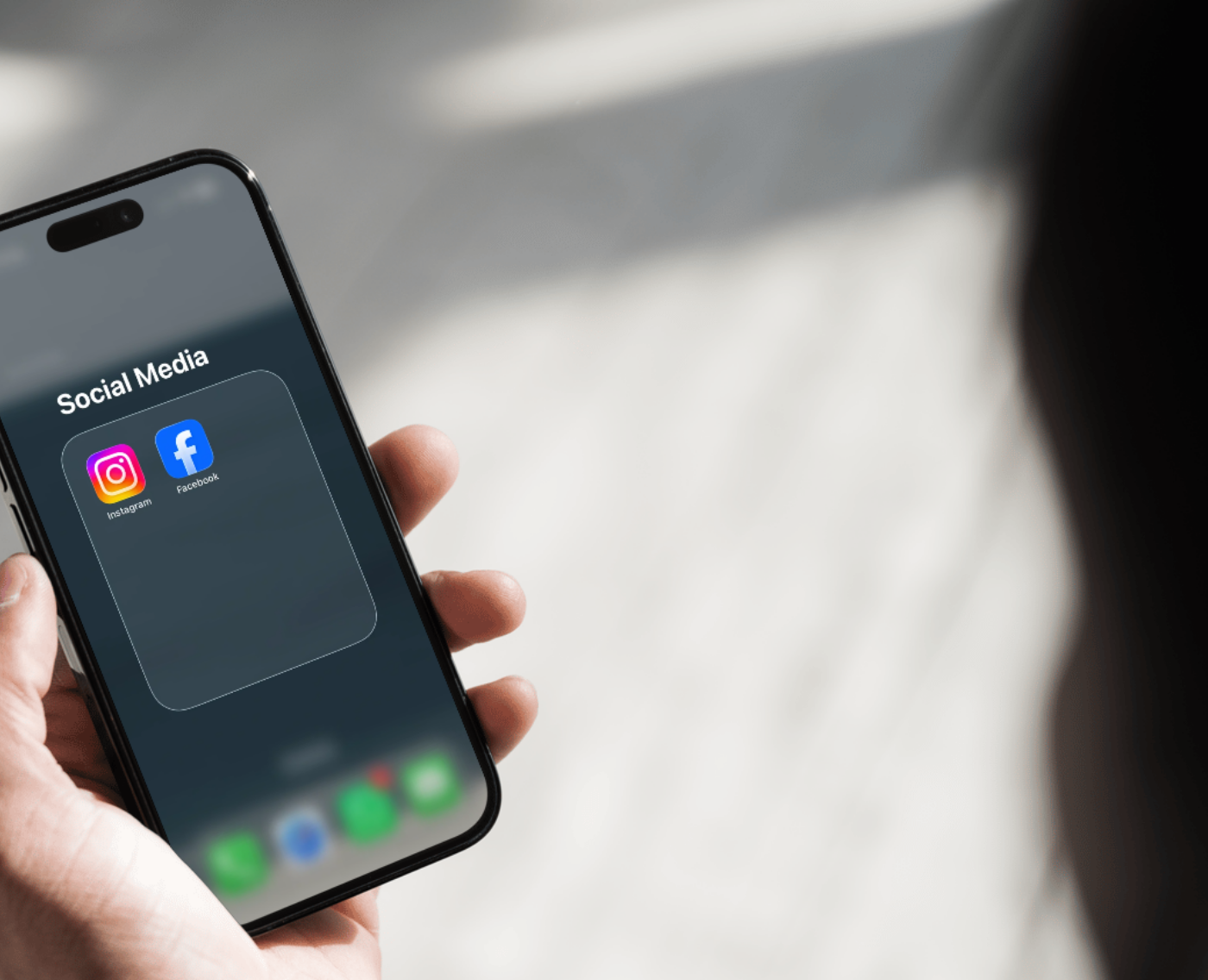 A person holds a smartphone displaying a "Social Media" folder containing the Instagram and Facebook apps, with the home screen dock visible below.